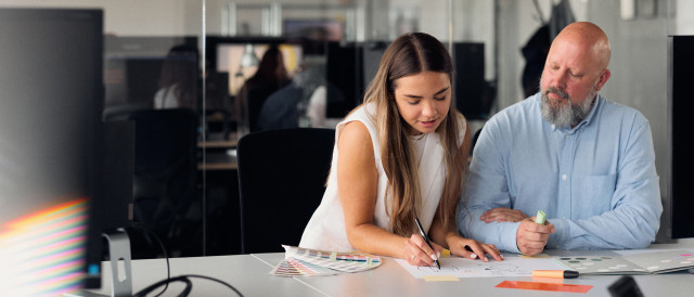 Zwei Personen skizzieren Ideen mit Farbfächern am Tisch